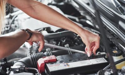 Replacing the battery. Car addicted woman repairs black car indoors in garage at daytime