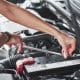 Replacing the battery. Car addicted woman repairs black car indoors in garage at daytime
