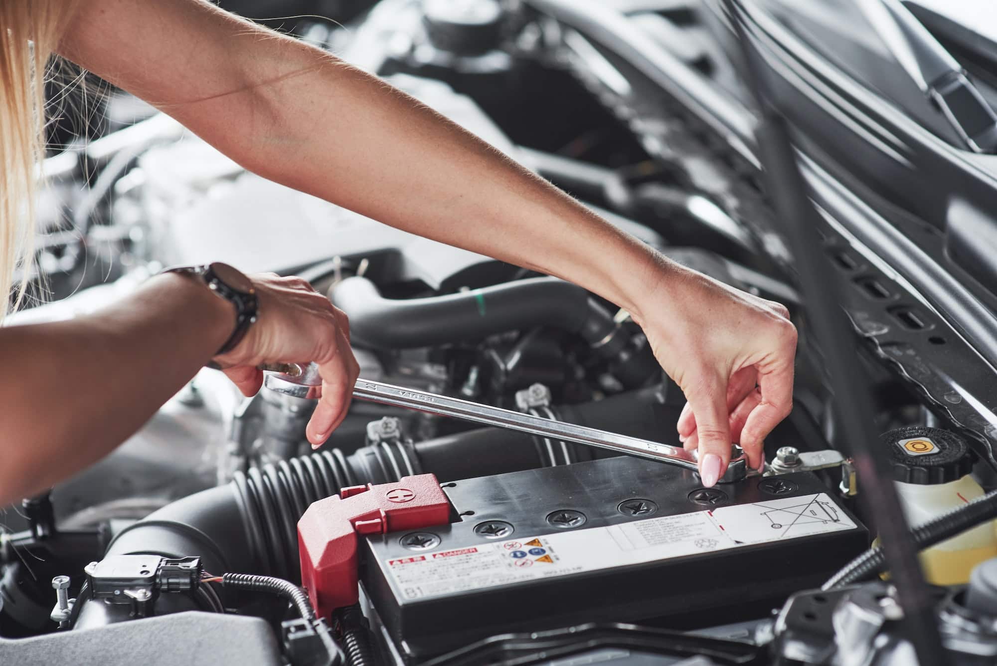 Replacing the battery. Car addicted woman repairs black car indoors in garage at daytime